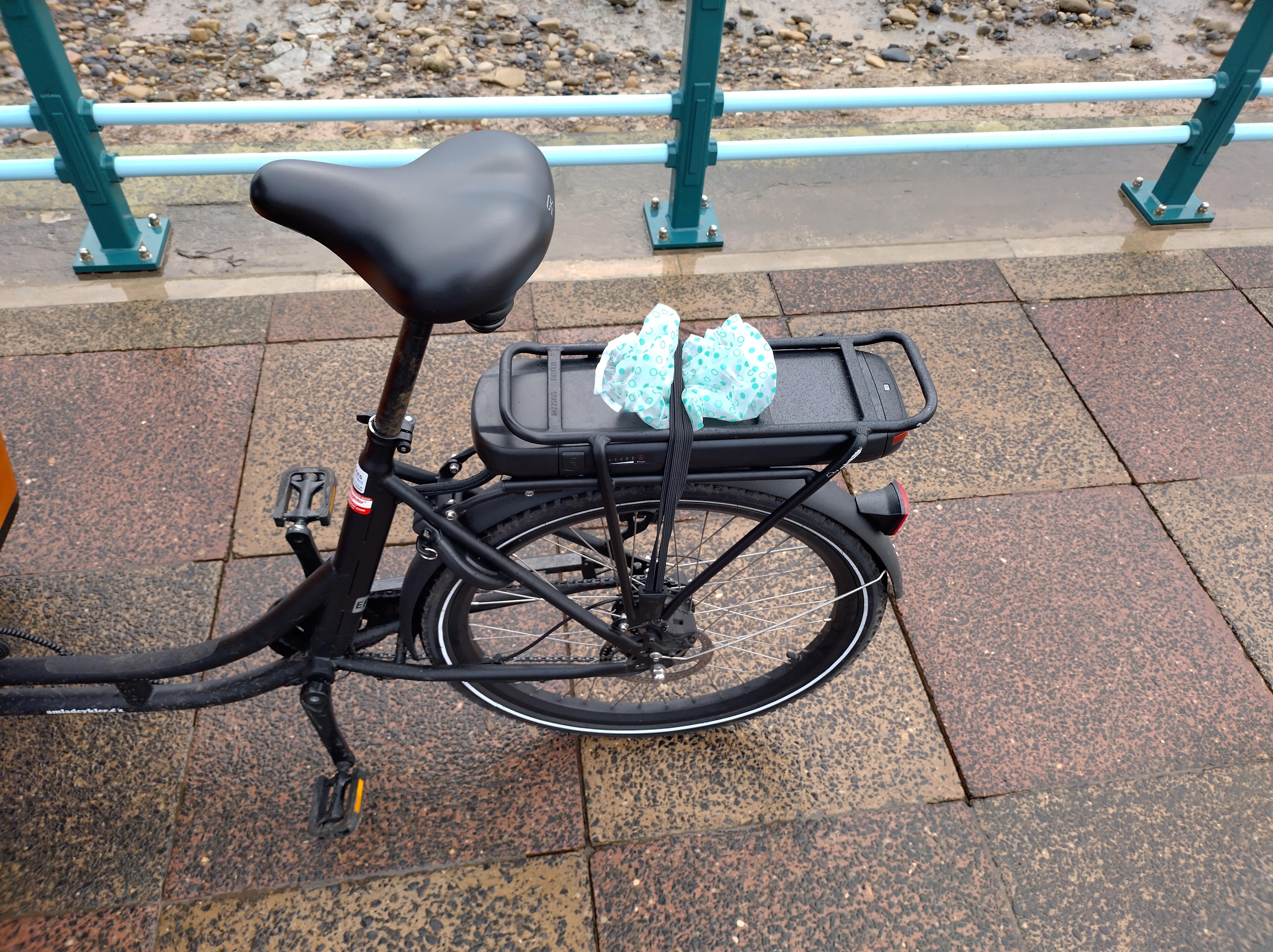 The back half of the bike, which looks like a normal bike. The battery is under the pannier rack, and the frame is step-through, curving down under the bucket.