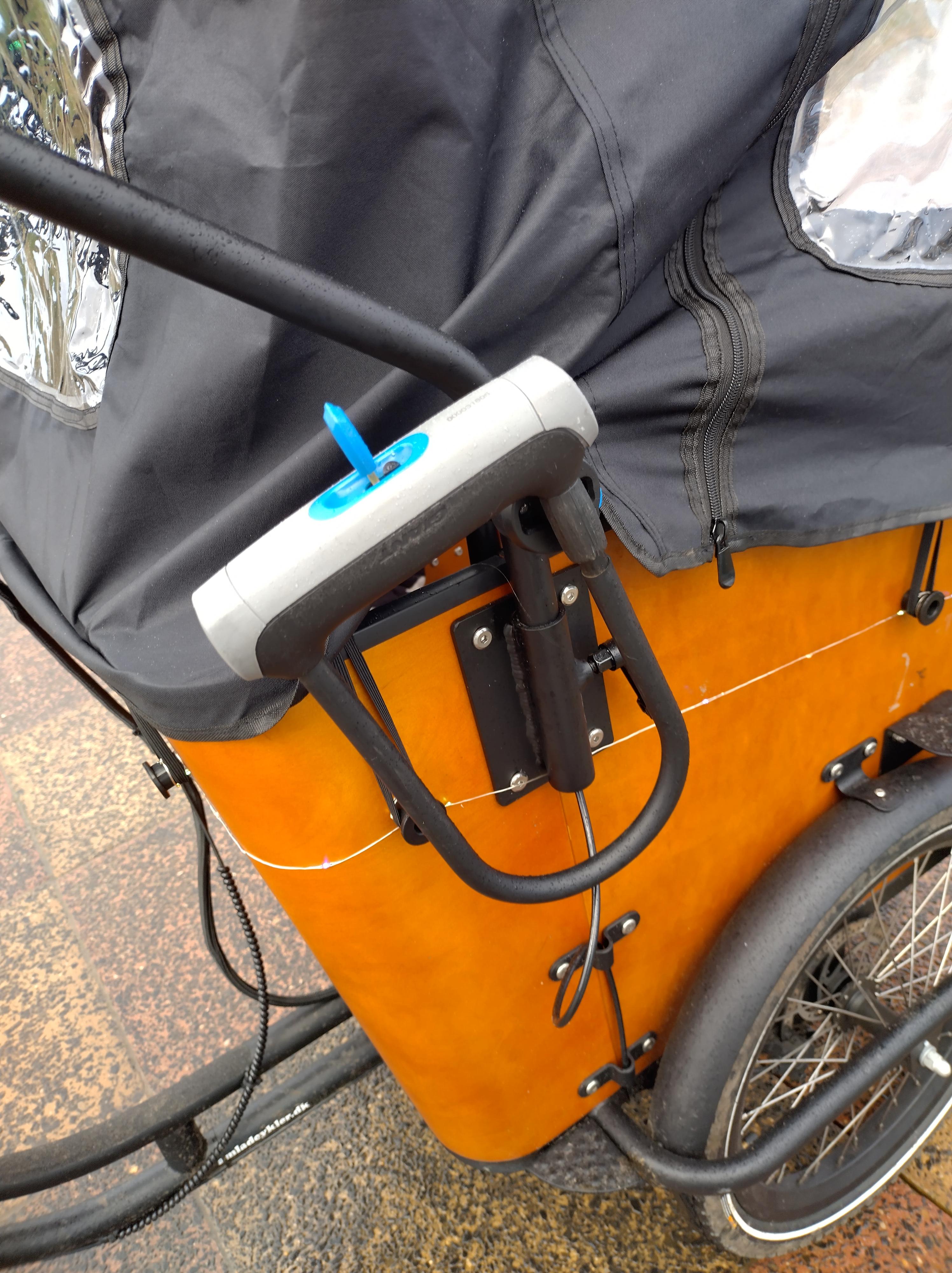 The D-Lock mounted to the vertical part of the handlebar on the side of the bike.