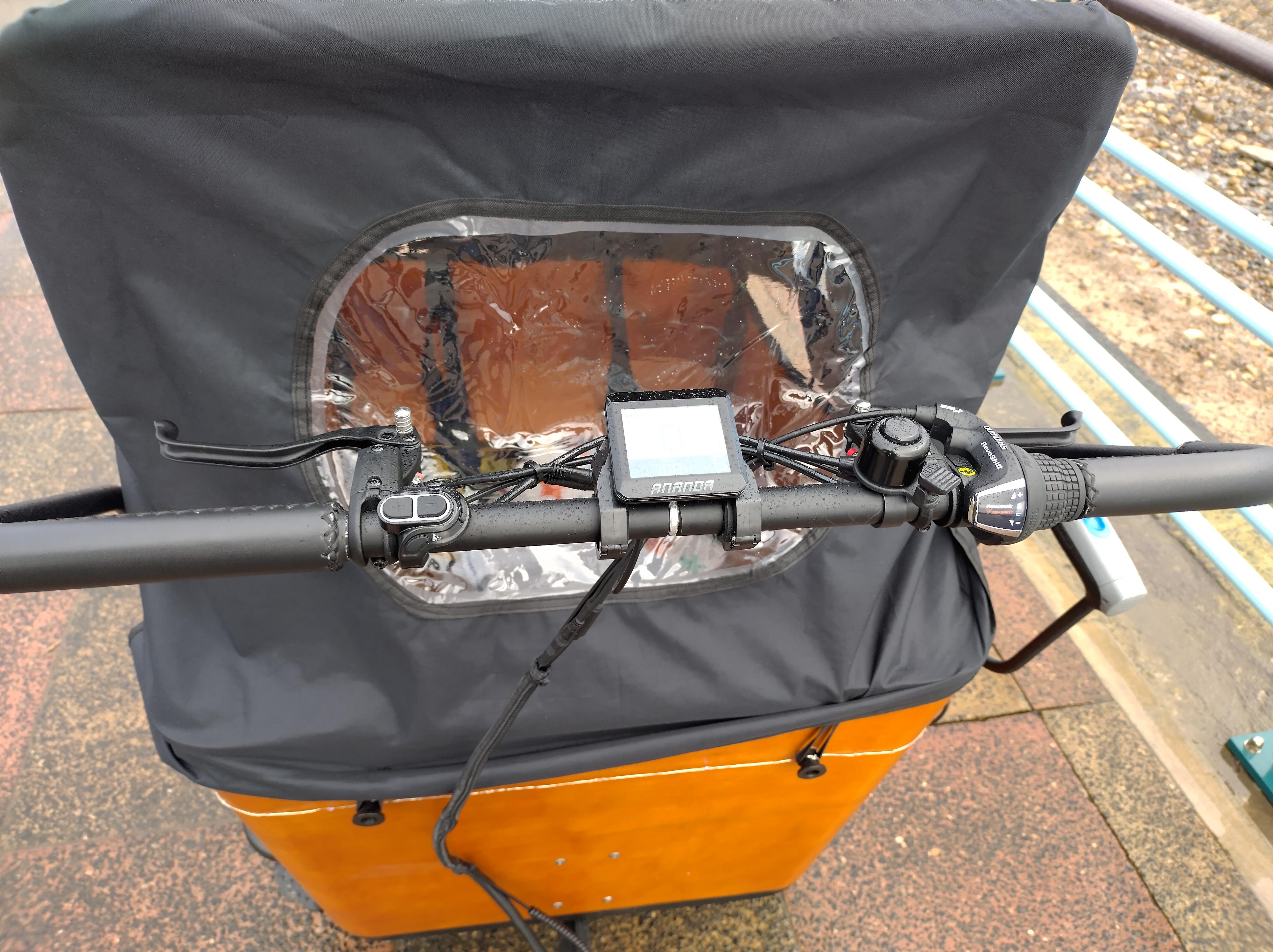 Looking from the rider's position down at the handlebar. It's a long horizontal bar, with the brake levers, gear changer, motor controls, motor display and ping bell arranged along it.